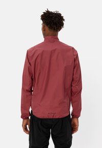 Bordeauxrote wasserdichte Jacke mit hohem Kragen, elastischen Bündchen und einem Kordelzug im Saum. Leichtes synthetisches Material mit mattem Finish.