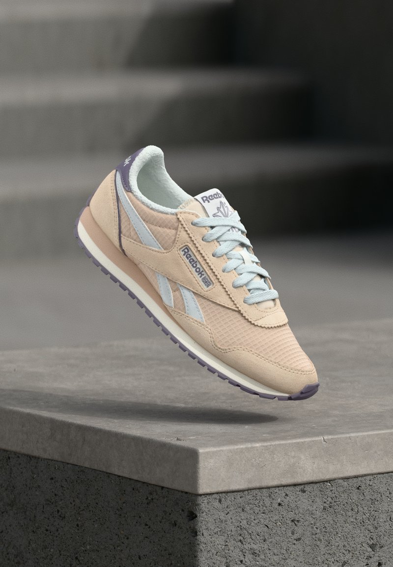 Beige un gai zilā Reebok kedas, kas flotē virs betona noma, ar betona kāpnēm fona.