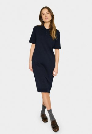 Rochie polo bleumarin cu mâneci scurte, croială până la genunchi și tiv cordat. Dispune de un guler cu trei nasturi și material texturat.