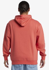 Korálová mikina s voľným strihom, nastaviteľnou kapucňou so šnúrkou, rebrovanými manžetami a lemom, vyrobená z mäkkého materiálu s hladkou textúrou.