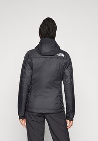 Osoba s pletenicama, obučena u crnu jaknu s kapuljačom marke North Face i odgovarajuće crne hlače, stoji okrenuta leđima prema kameri.