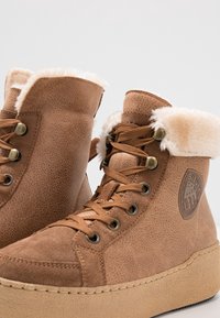 Bottes d'hiver montantes marron avec doublure en fausse fourrure, lacets sur le devant, cuir texturé et patch de marque sur le côté.