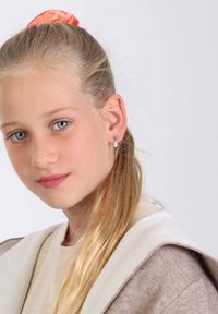 Boucles d'oreilles en argent au design circulaire avec une petite pierre précieuse. Cheveux châtains clairs partiellement attachés avec un chouchou pêche.