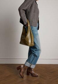 Stivaletti alla caviglia in pelle di serpente marrone, jeans blu rilassati con dettagli a risvolto e una borsa a spalla in pelle verde oliva liscia. Giacca grigia con texture.