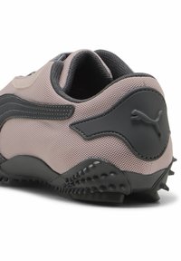 Helle rosa Sneaker mit schwarzen Akzenten, strukturiertem Mesh-Obermaterial und Gummisohle mit Spitzen für besseren Halt. Puma-Logo an der Seite.