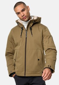 Giacca isolante verde oliva con zip frontale, cappuccio regolabile e due tasche frontali. Presenta accessori neri e una morbida fodera interna.