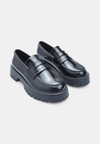 Mocasines de charol negro con suela de goma gruesa, que presentan una doble correa en el empeine y un acabado brillante.