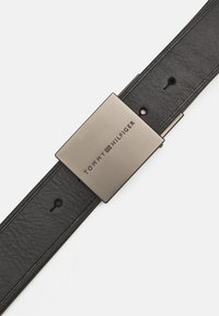 Cinturón de cuero negro con hebilla metálica rectangular grabada con "TOMMY HILFIGER". Ajustable con múltiples orificios para un mejor ajuste.