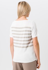 White t-shirt featuring horizontal beige stripes across the back. Short sleeves and a relaxed fit with a round neckline.