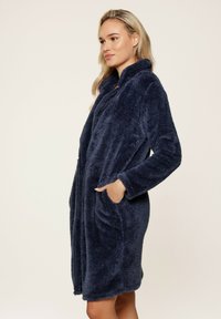 Robe en velours bleu marine, long, avec une texture douce, un col châle et deux poches avant. Design mi-long avec une coupe décontractée.