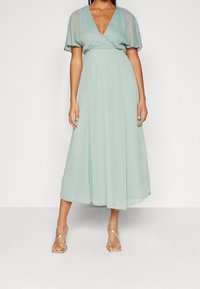 Robe longue vert clair, avec de courtes manches flottantes, un décolleté en V profond et un design enroulé, fabriquée dans un tissu fluide et texturé.