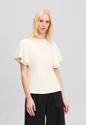 Helebeige lühikeste varrukatega topp flared varrukatega, sile tekstuur, ümmargune kaelus ja kitsas siluett, koos mustade laiade pükstega.