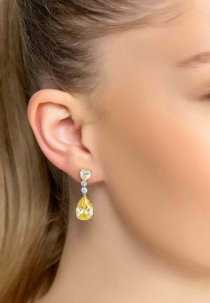 Yellow and clear gemstone earrings with a teardrop shape and heart-shaped accents, set in silver-colored metal.