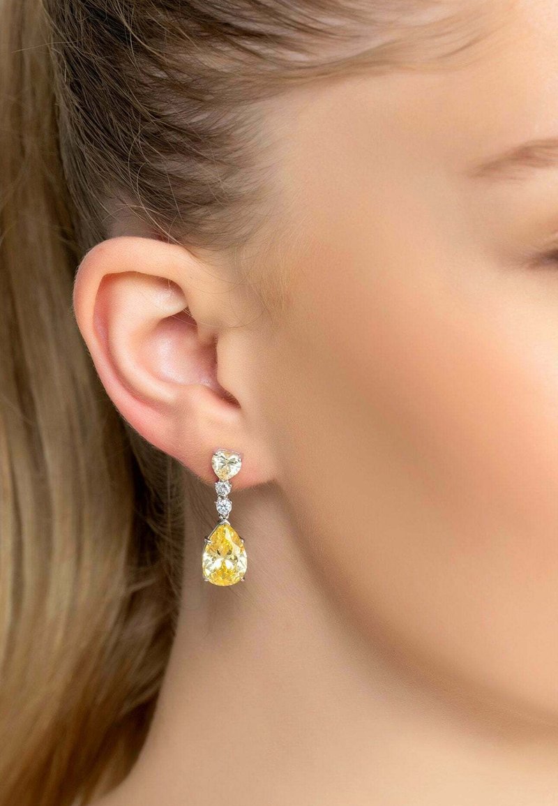 Yellow and clear gemstone earrings with a teardrop shape and heart-shaped accents, set in silver-colored metal.