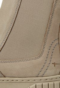 Beige suede ankle boot with ribbed fabric panel, contrasting stitching, and rubber sole. Features subtle accents and a textured surface.