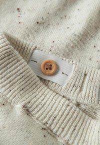 Gros plan sur un tissu en maille beige avec un motif moucheté, présentant une taille ajustable avec un bouton en bois sur un élastique.