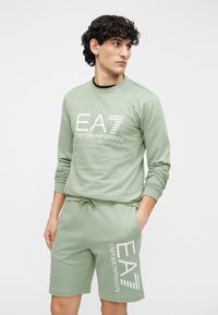 Lichtgroene sweatshirt met lange mouwen en een wit logo; bijpassende korte broek met een elastische tailleband en logodetail aan de zijkant.