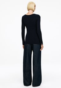 Marineblaues, geripptes Langarmoberteil mit rundem Rückenausschnitt, kombiniert mit weit geschnittenen, dunklen Jeanshosen, die eine lässige Passform und leichte Strukturvariationen aufweisen.