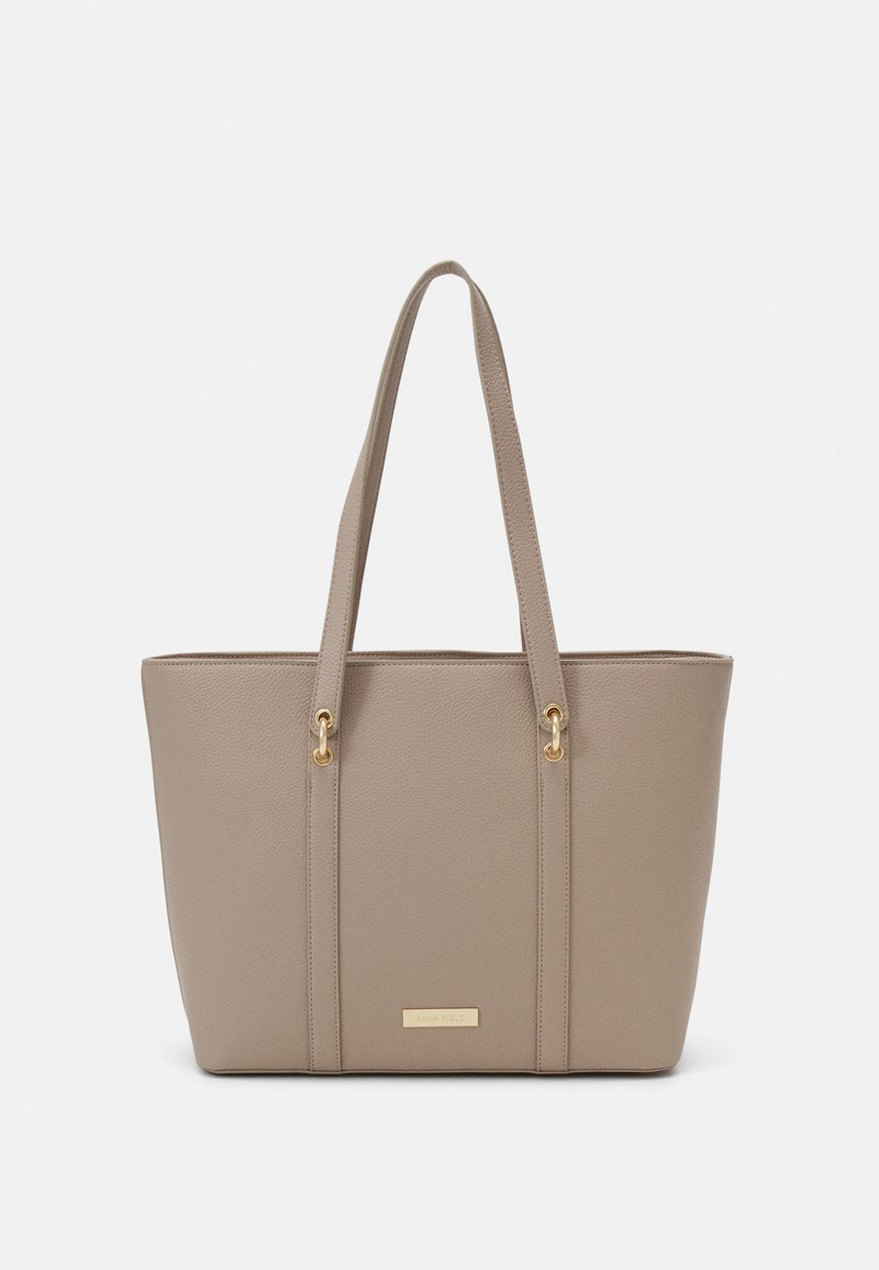 Beige tote taske lavet af tekstureret materiale med to skulderremme. Har guldfarvet hardware og en plade på fronten.