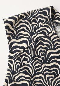 Tessuto a motivi nero e crema con strisce ondulate. La superficie appare morbida e lavorata a maglia, con un colletto sulla parte superiore.