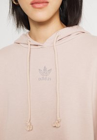 Rožā kapuce, kas izgatavota no mīksta auduma ar auklu. Uz krūtīm ir Adidasa logo, rotāts ar rhinestone akmeņiem.