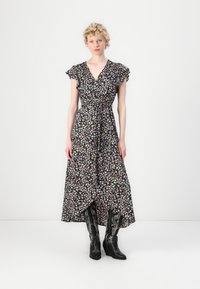 Robe portefeuille à fleurs avec de courtes manches volantées, fond noir, fleurs roses et bleues, taille ceinturée et ourlet longueur cheville. Associée à des bottes de cowboy noires.