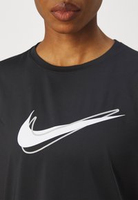 Must tumes mustri kangas, millel on esipinnal silmapaistev valge Nike swoosh logo.