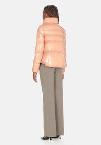 Giacca a vento padded rosa lucido, colletto alto, con cuciture orizzontali. Indossata con pantaloni grigi chiari a gamba larga e tacchi neri.