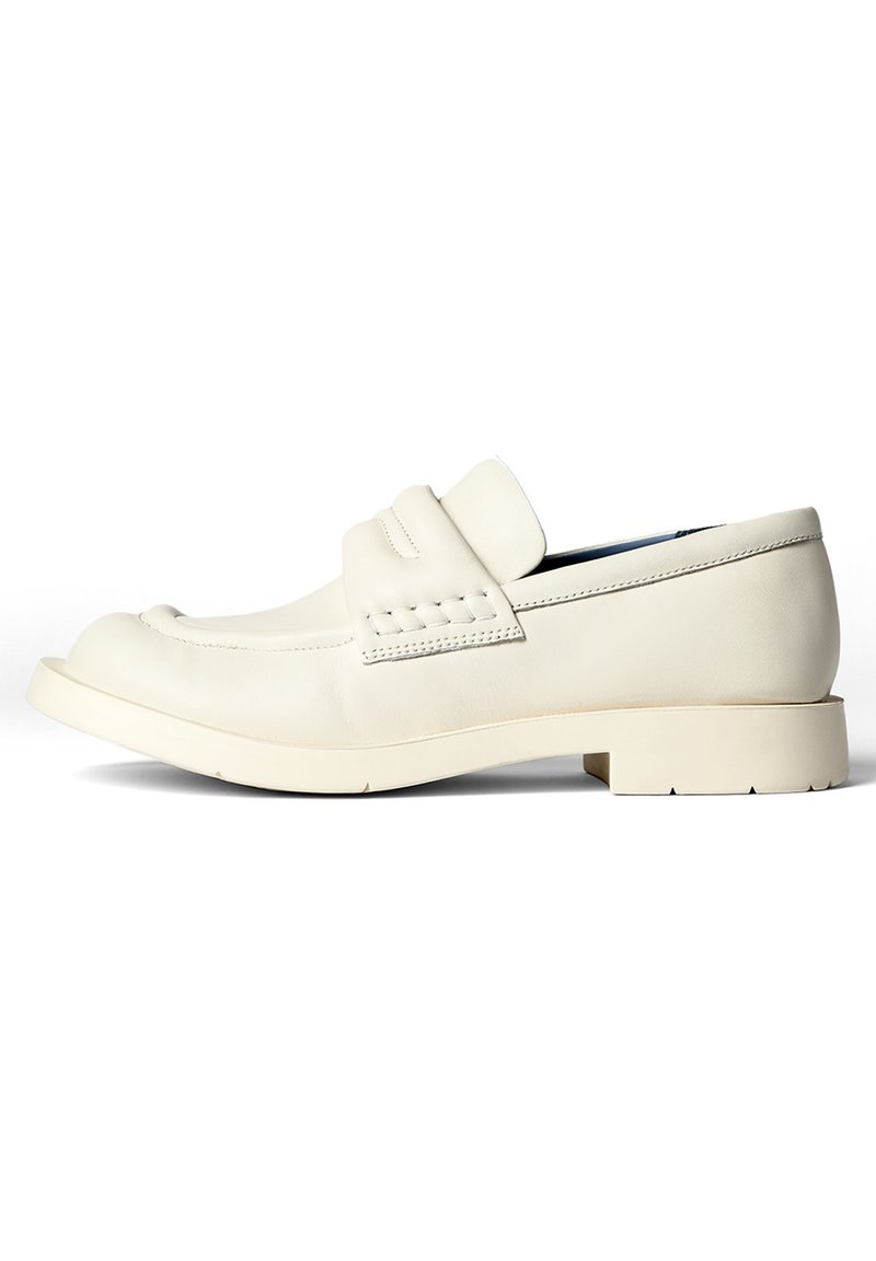 White leather loafer with a rounded toe, featuring a decorative strap and stitching details. Flat rubber sole with a textured finish.