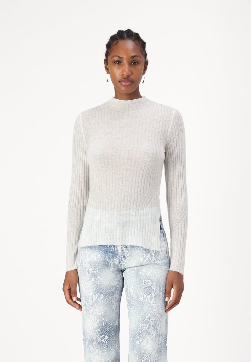 Lys grå ribbestrikket genser med høy hals, med en gradienthem og sideslitser. Kombinert med lys blå jeans med slangeprint.
