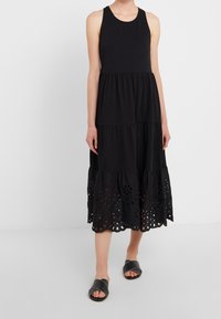 Černé bezramínkové šaty s vrstveným designem, s krajkovým lemem broderie anglaise. Vyrobeny z měkkého materiálu, který poskytuje uvolněný fit. Nosené s černými pantoflemi.