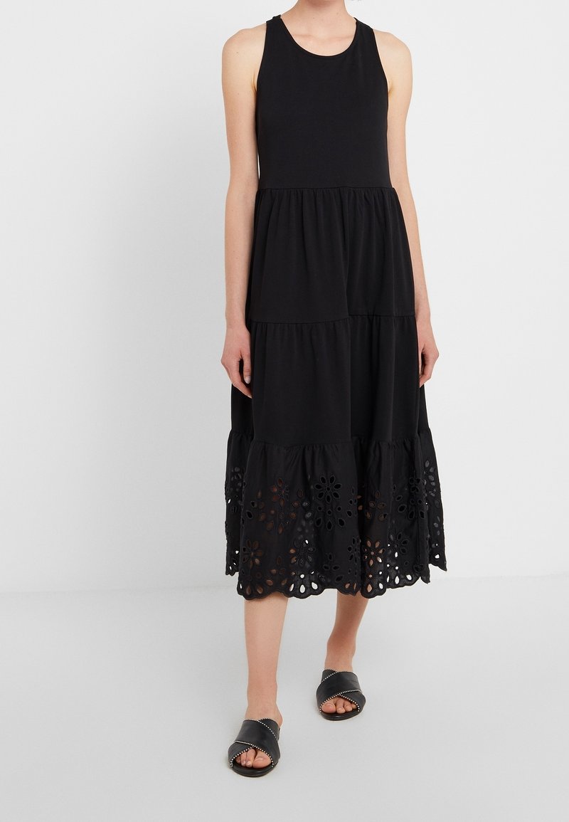 Černé bezramínkové šaty s vrstveným designem, s krajkovým lemem broderie anglaise. Vyrobeny z měkkého materiálu, který poskytuje uvolněný fit. Nosené s černými pantoflemi.