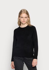 Black sweater made of soft material with a round neckline, ribbed cuffs, and hem. Worn with dark gray jeans for a casual look.