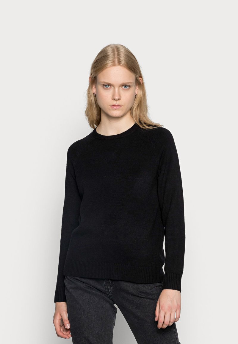 Black sweater made of soft material with a round neckline, ribbed cuffs, and hem. Worn with dark gray jeans for a casual look.