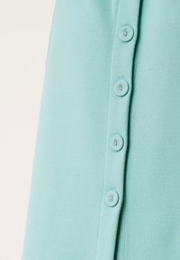 Tessuto verde acqua chiaro con una fila verticale di cinque bottoni coordinati con una leggera lucentezza, che mette in risalto una texture liscia e un design semplice.