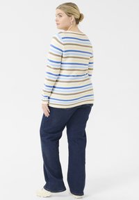 Striped long-sleeve top in beige, blue, and brown. Paired with navy blue jeans. Features a round neckline and ribbed texture.