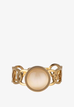 Anillo de oro con una piedra circular, que presenta una textura lisa y acentos unidos. Mano descansando suavemente sobre la piel, con un fondo neutro.