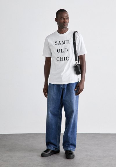 White t-shirt with black text "SAME OLD CHIC," paired with loose blue denim jeans and black sneakers. Small black crossbody bag.