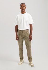Hvit bomulls T-skjorte med korte ermer, kombinert med taupe cargo bukser med sidelommer. Tilbehøret inkluderer lyse joggesko.