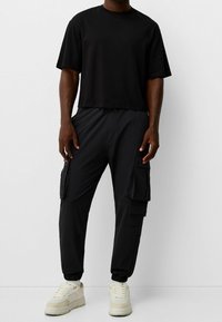 Svart kortärmad tröja och svarta cargobyxor med flera fickor, med elastiska muddar och dragsko i midjan. Vita sneakers fulländar looken.