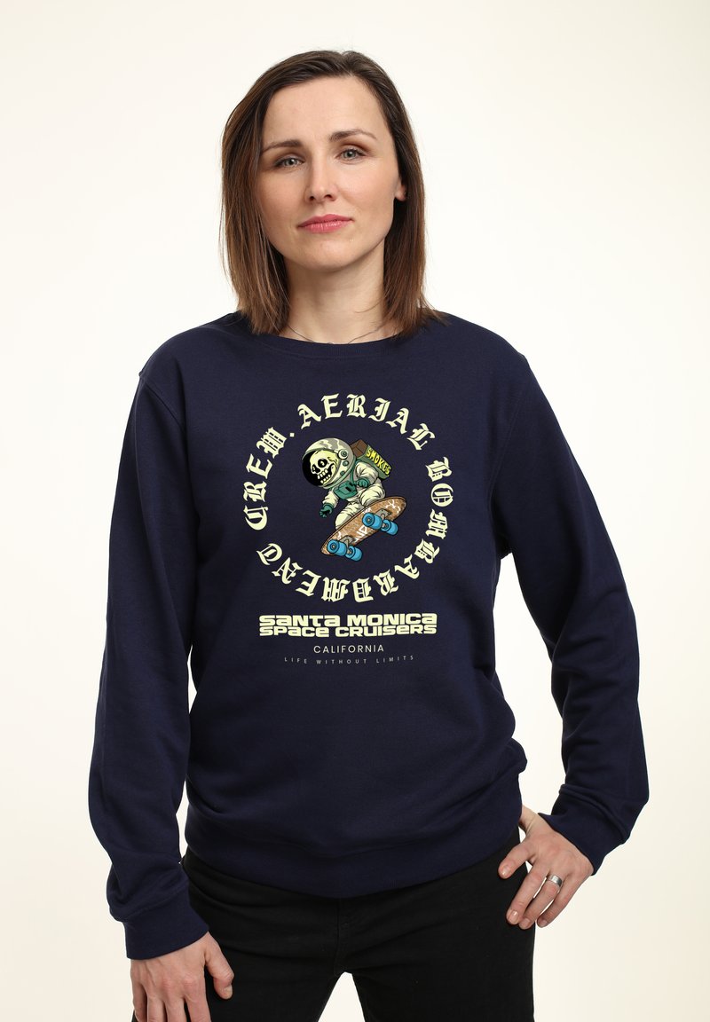 Felpa navy in cotone, con una stampa grafica di uno scheletro che fa skateboard, con testo e logo in crema e verde.