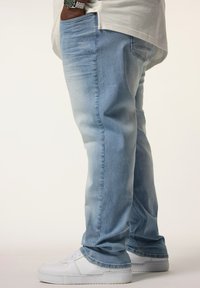 Jeans de mezclilla azul claro con corte recto, que presentan bolsillos frontales, detalles en el bolsillo trasero y una textura desgastada, combinados con zapatillas blancas.
