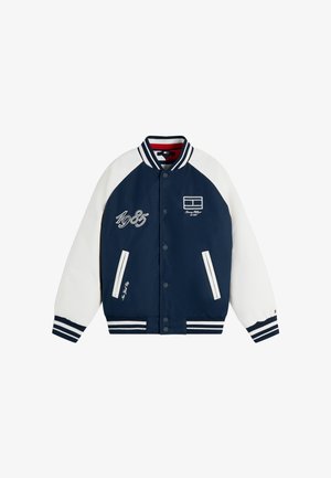 Marineblå og hvid varsityjakke med stribet krave og manchetter, forreste trykknapper, forlommer og "1985" broderi på brystet.