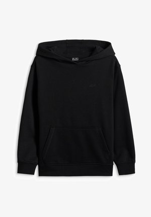 Garçon portant un bonnet bleu, un sweat à capuche noir, un sous-vêtement blanc, un pantalon cargo marron et des baskets noires et blanches, debout et souriant.
