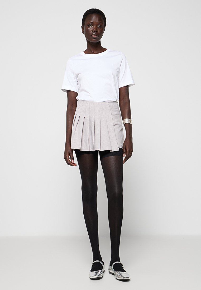 Szara plisowana spódnica z dopasowanym pasem, w połączeniu z białą koszulką z krótkim rękawem. Czarny rajstopy i srebrne buty dopełniają wygląd.