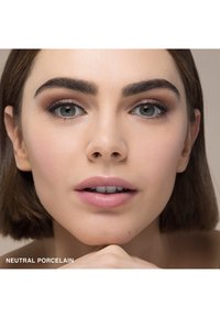Nahaufnahme eines glatten, hellen Hauttons, beschriftet mit "Neutral Porcelain", mit ordentlich geformten, dunklen Augenbrauen und sanft pinken Lippen auf einem neutralen Hintergrund.
