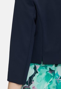 Granatowa marynarka z trzema ćwierć rękawami, gładką teksturą, dopasowanym krojem i subtelnym rozcięciem z tyłu, w połączeniu z spódnicą w kwiatowy wzór.