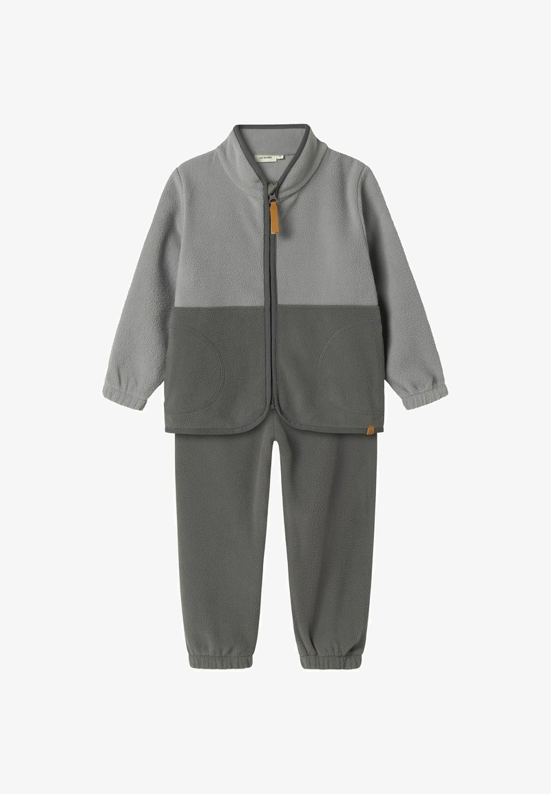 Kergedest ja tumedast hallist fliist treeningkostüüm. Selles on lukkudega jakk kõrge kraega ja kaks ümmargust taskut. Püksid elastsete sääreotstega.