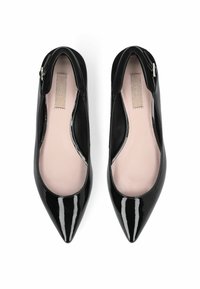 Ballerines en cuir verni noir avec un bout pointu, un design épuré et un détail en découpes sur le côté. Intérieur doublé de beige clair.