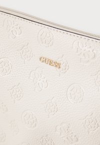 Pochette en cuir texturé crème avec logos embossés, dotée d'un badge doré "GUESS!" et d'une fermeture éclair. Des détails de motif subtils améliorent son design.